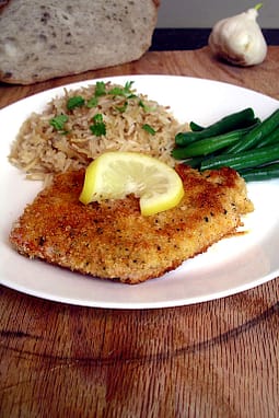 a breaded pork cutlet on a white plate with rice pilaf and green beans